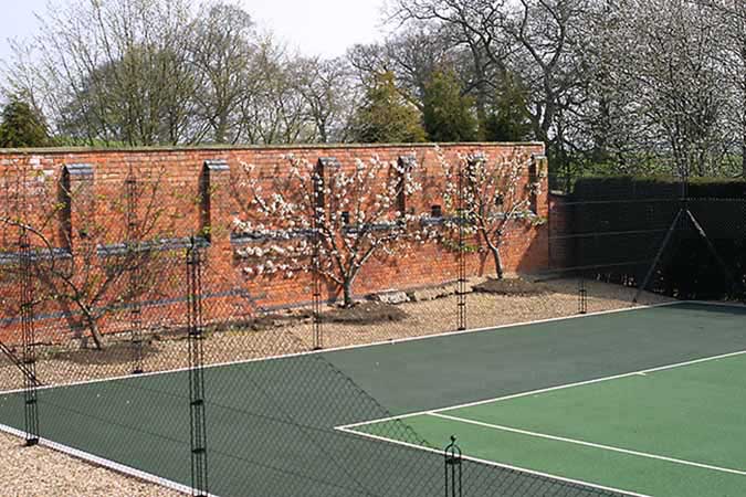 A Matchplay tennis court from En Tout Cas with patented Obelisk fencing framed by an old brick wall